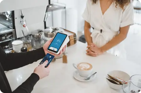 Merchant holding a Point of Sale Device as they make a sale to a customer